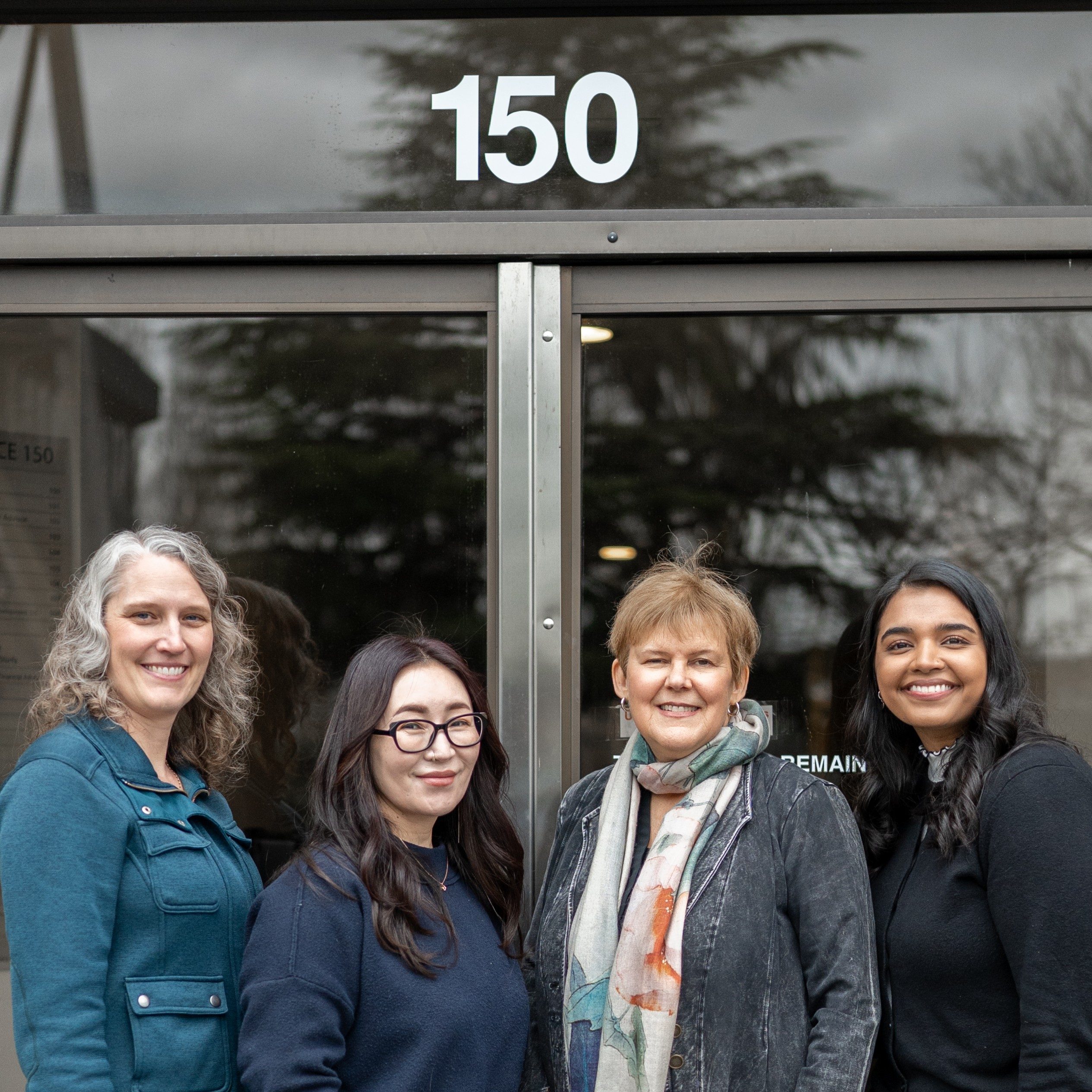 A picture of four team members outside the office's front doors. "150" is shown on the front of the building